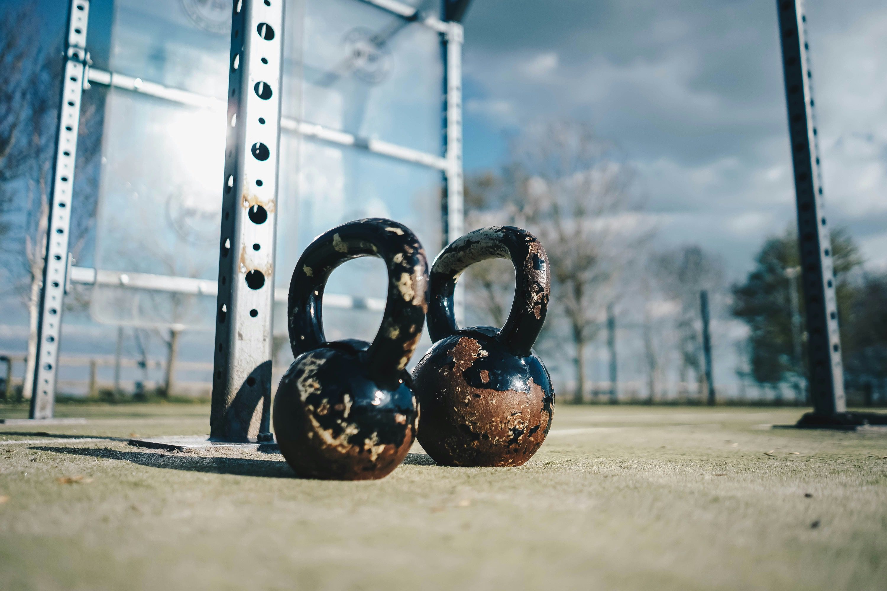 Two rusty kettlebells on a concrete floor outdoors.