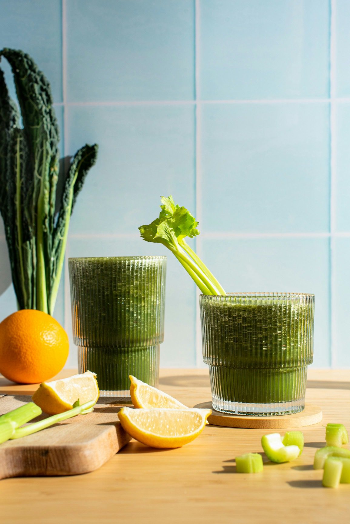 Two green smoothies with celery and lemon slices on a table.